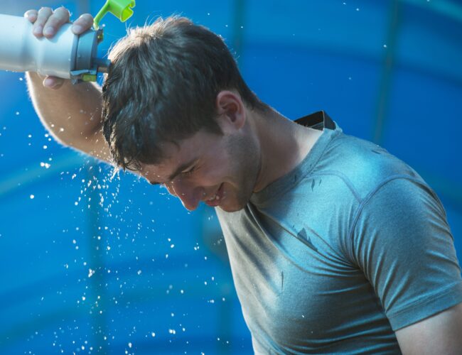 Young tired athlete splashing and pouring fresh water on his head to refresh during a running trail